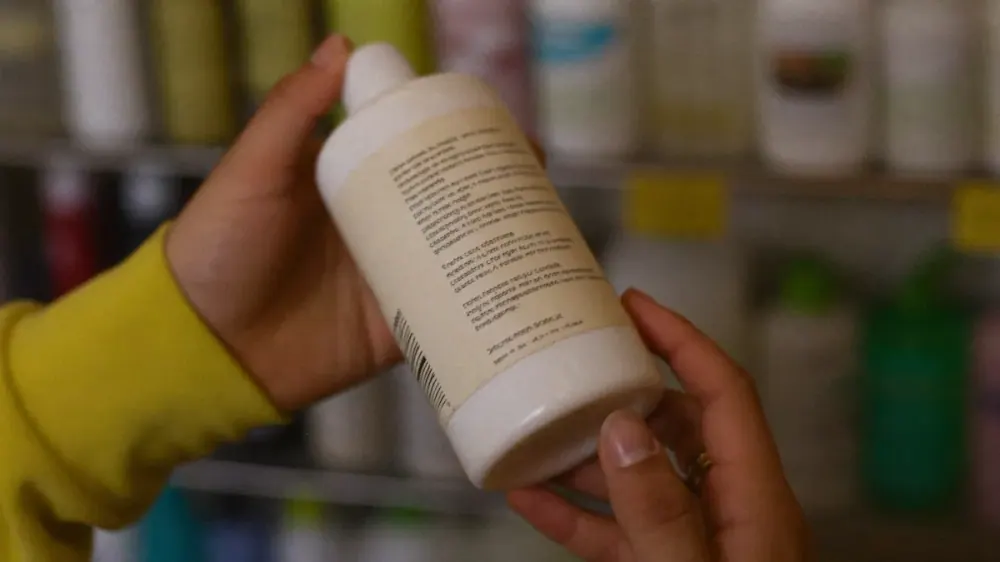 Manos girando un bote de champú para leer la lista de ingredientes INCI de la etiqueta trasera