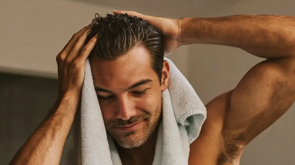 Hombre secándose el pelo mojado presionando suavemente con una toalla de microfibra en lugar de frotar